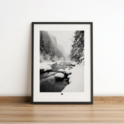 Black and white photo of a river surrounded by fir trees in the mountains. Modern, designer winter wall hanging.
