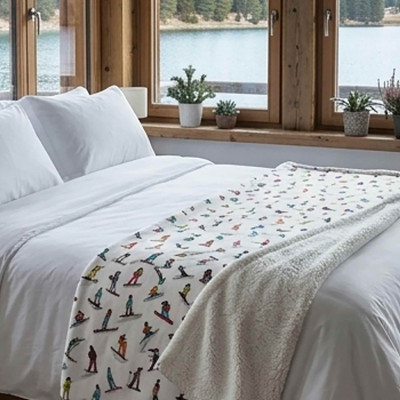 XL white throw blanket placed on a bed in a bedroom. Soft and thick blanket featuring colorful skiers.